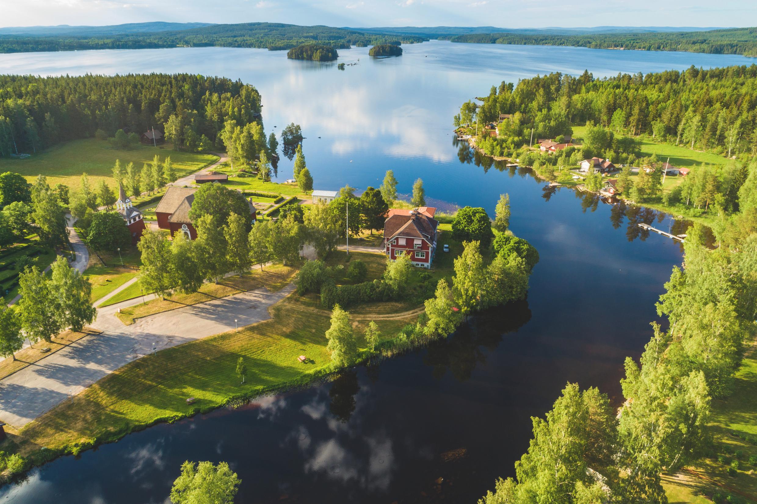 An aerial view of a river that leads to Toftan Lake. There is a red house near the water surrounded by greenery.