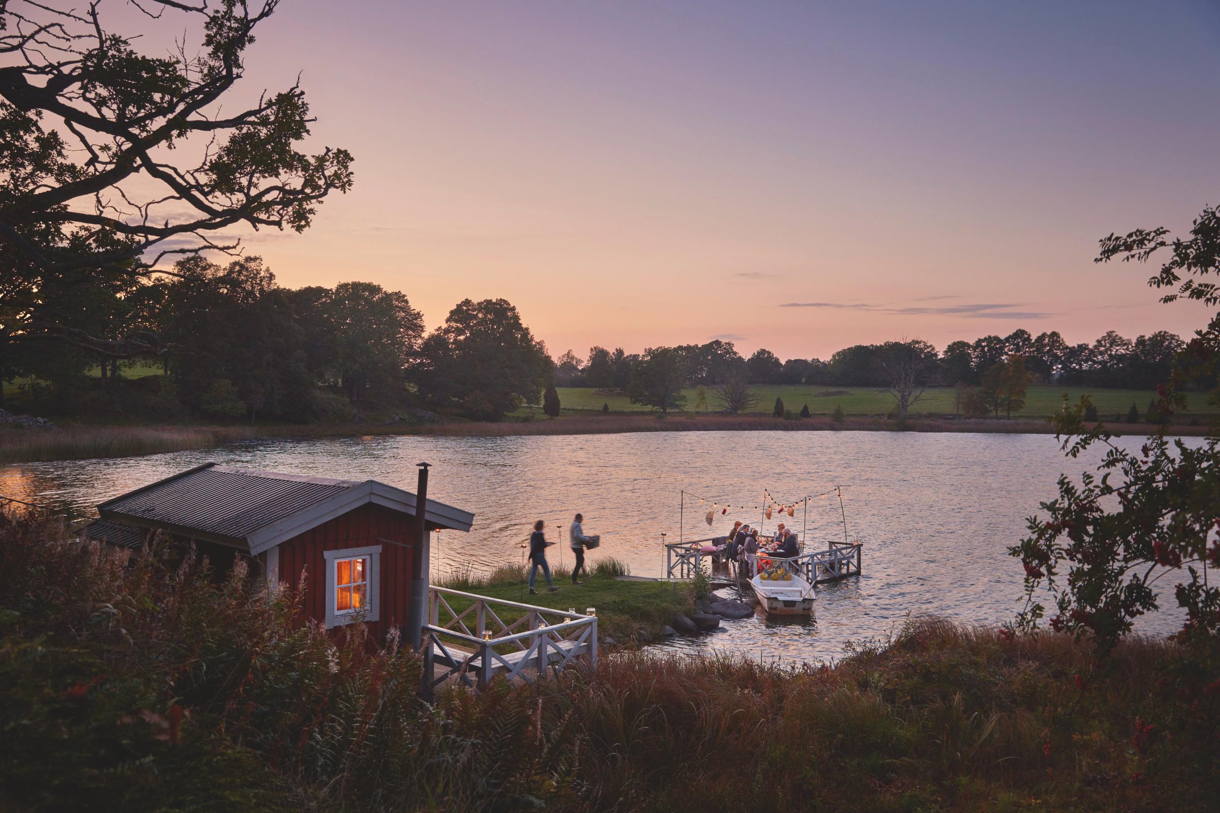 People having a Swedish crayfish dinner on a small jetty in a lake at dusk.