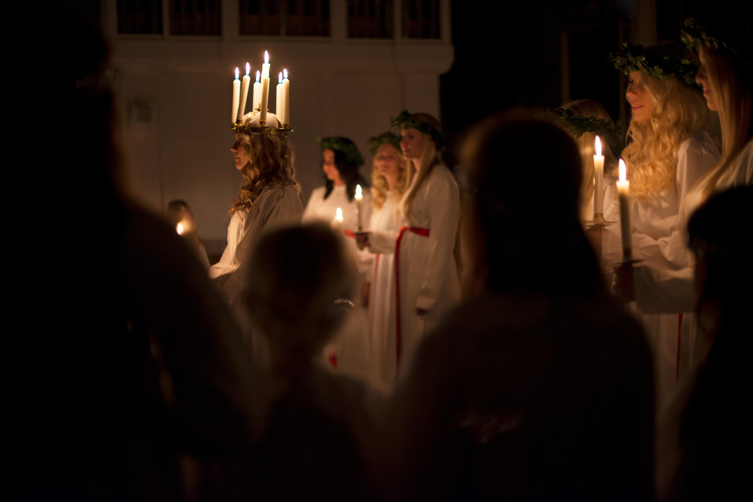 لوسيا وعلى رأسها إكليل من الشموع المضاءة ويقف خلفها الخادمات وهن يحملن في أيديهن شمعة مضاءة.