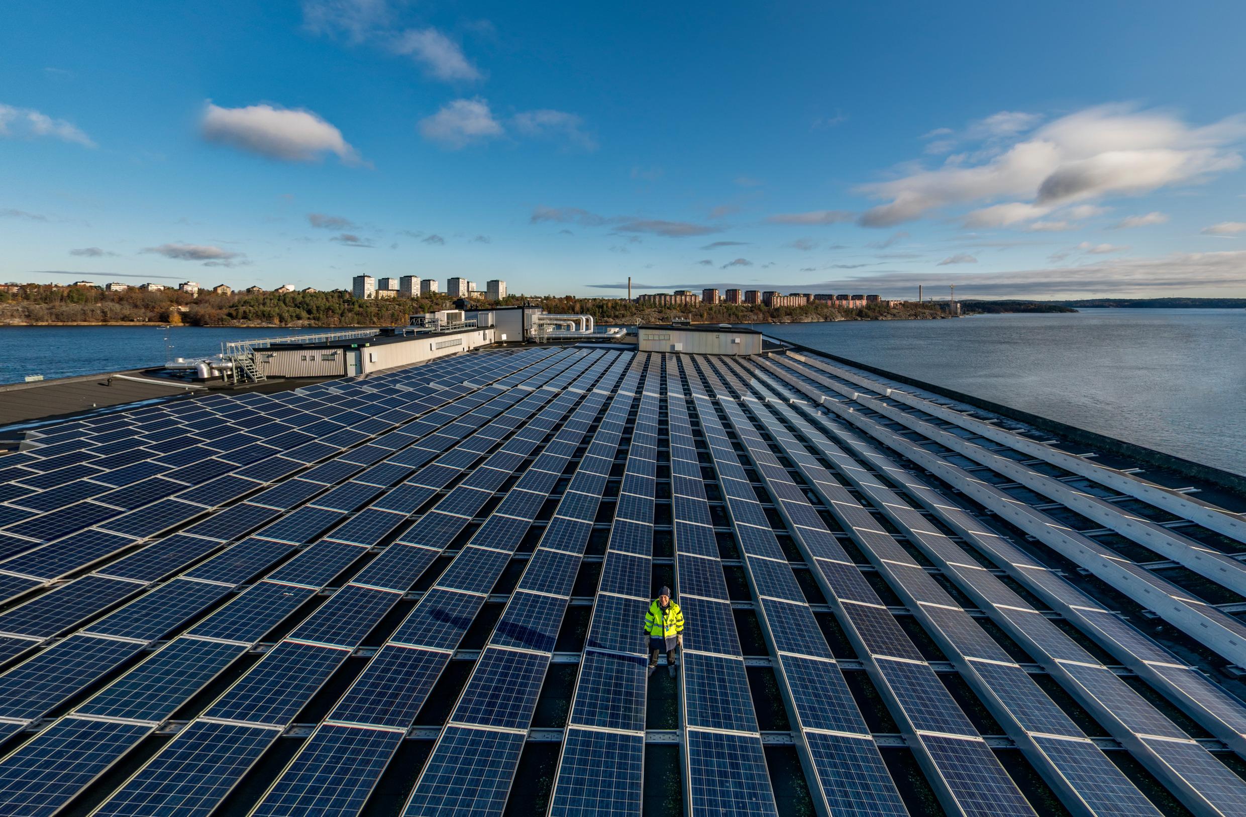 منشأة ضخمة للطاقة الشمسية في السويد على سطح أحد الأبنية، خلفها مسطح مائي كبير وأحد المدن.